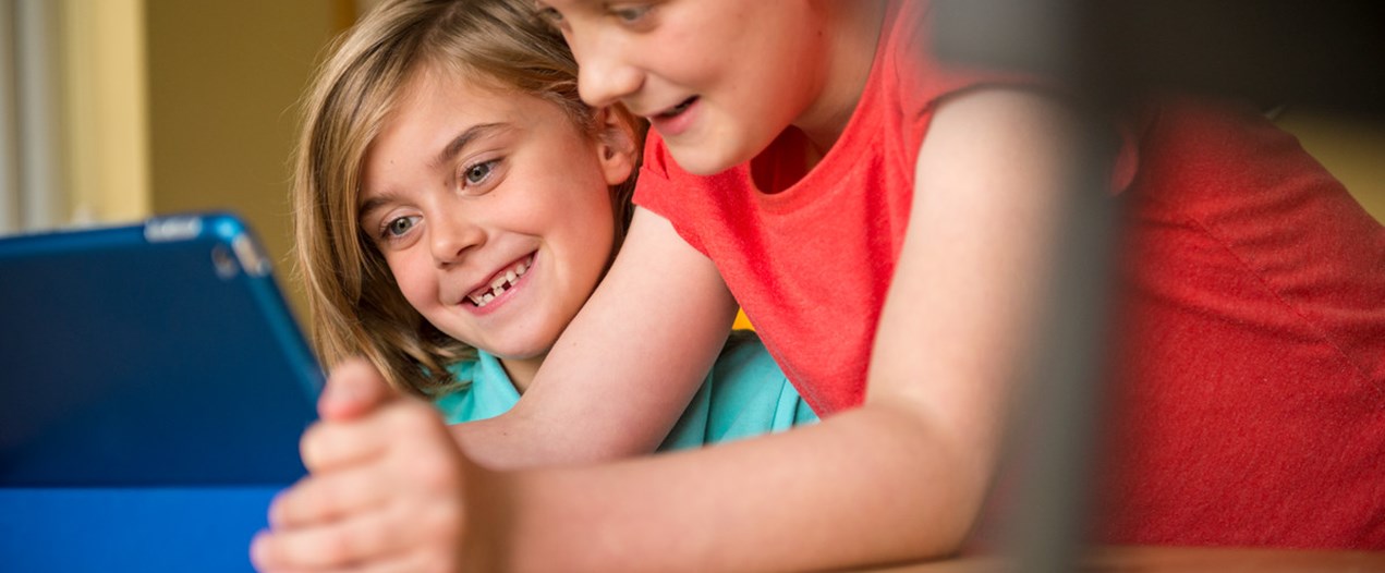 Family home_Two children leaning on a desk looking at a tablet and laughing._At home.jpg