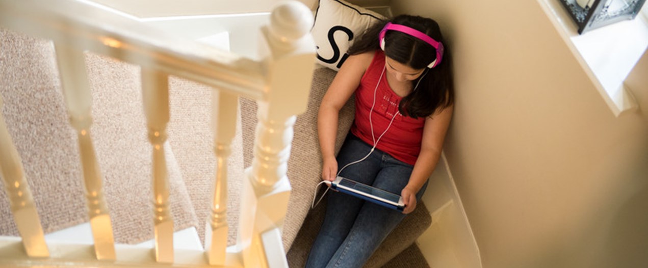Family home _Young girl sat on the stairs with headphones on plugged into her tablet. Photo taken from birds eye view. _At home.jpg