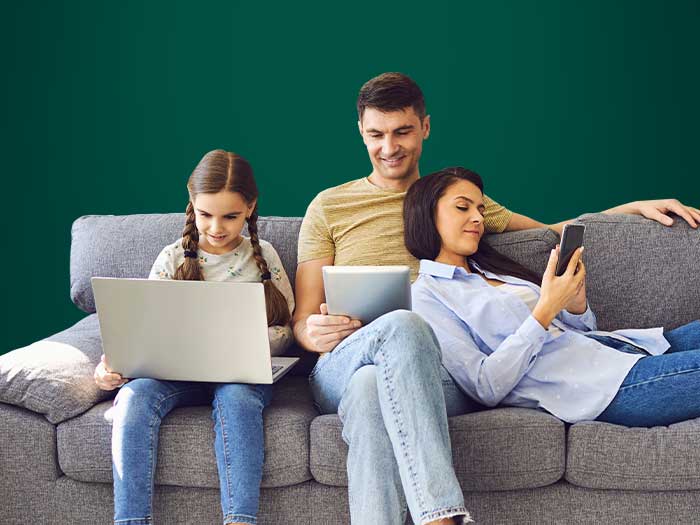 A family relaxing on the sofa and each using different devices - mobile, tablet and laptop - to use the internet.