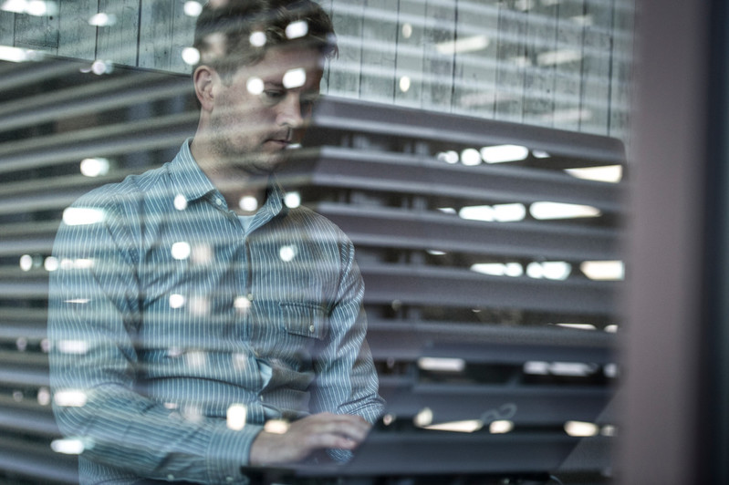 A man diligently focused on his laptop, engrossed in work within an office environment.