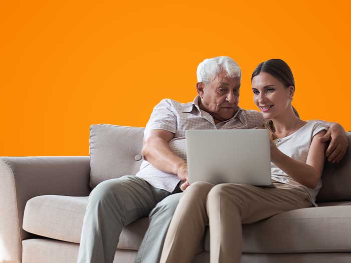 A woman and elderly man sitting on sofa and looking at laptop together.