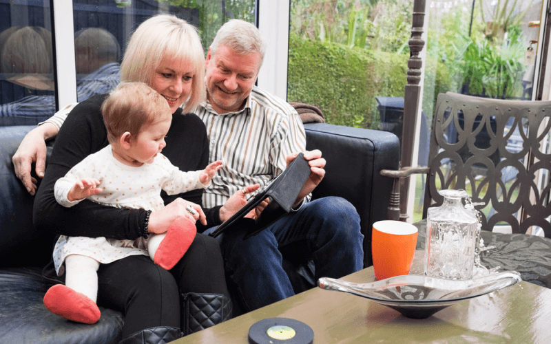 Man and women with toddler sat on a couch using tablet.