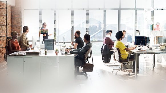 Open office space designed with an open-plan layout, showcasing colleagues engaged in various tasks across the shared workspace. This scene highlights the dynamic environment where employees collaborate, multitask, and interact in a flexible and communal setting.