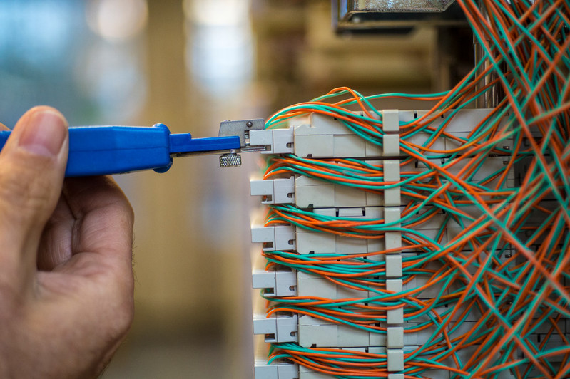 The image portrays a man holding equipment while engaged in the process of fixing or installing network cables, highlighting his technical expertise in networking.