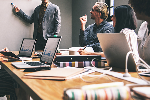 In a professional business meeting, a man is taking charge of the presentation, holding a marker pen to emphasize a crucial point on the display as his colleagues engage attentively.