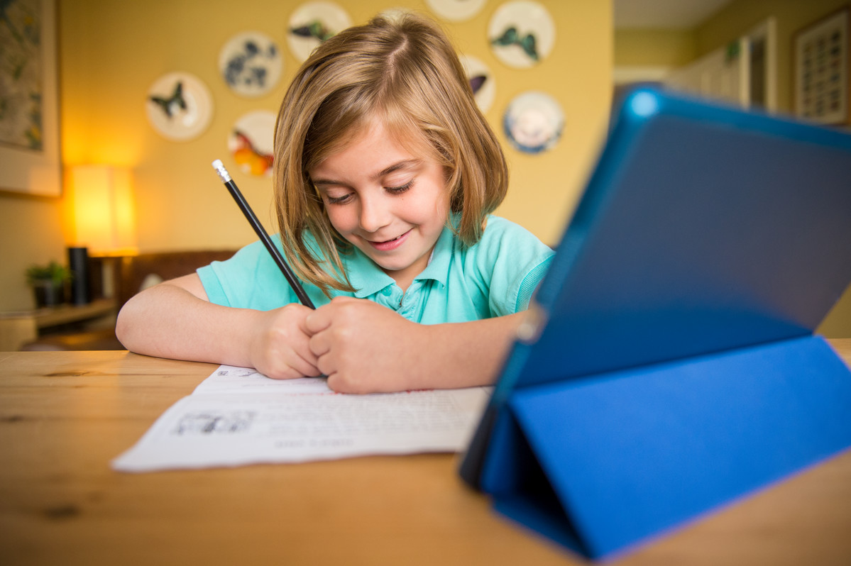 Young girl leaning on a desk writing with a tablet in front of her at home