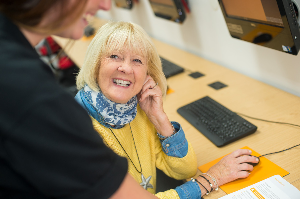 Smiling woman at a KCOM Get online session with hand on computer mouse.